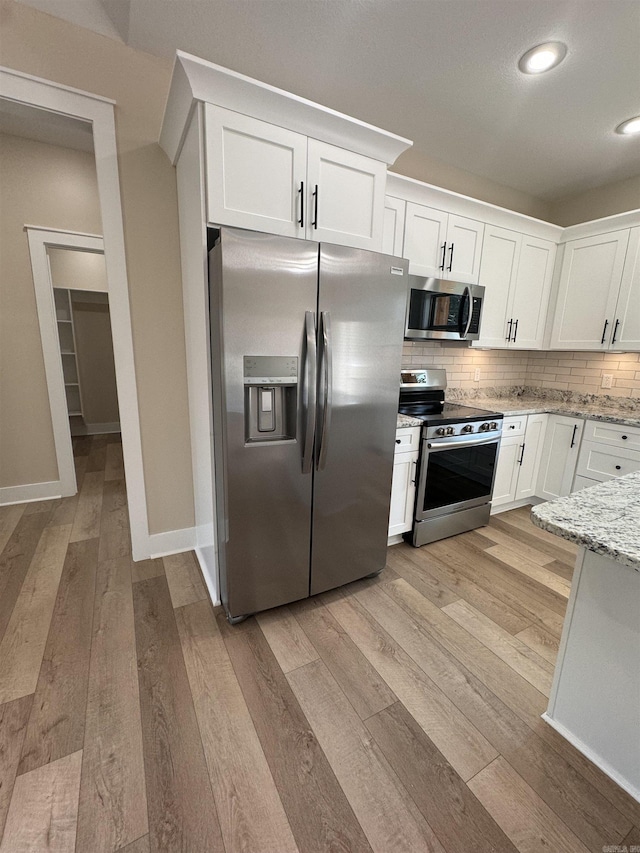 kitchen with light stone countertops, light hardwood / wood-style flooring, decorative backsplash, white cabinetry, and appliances with stainless steel finishes