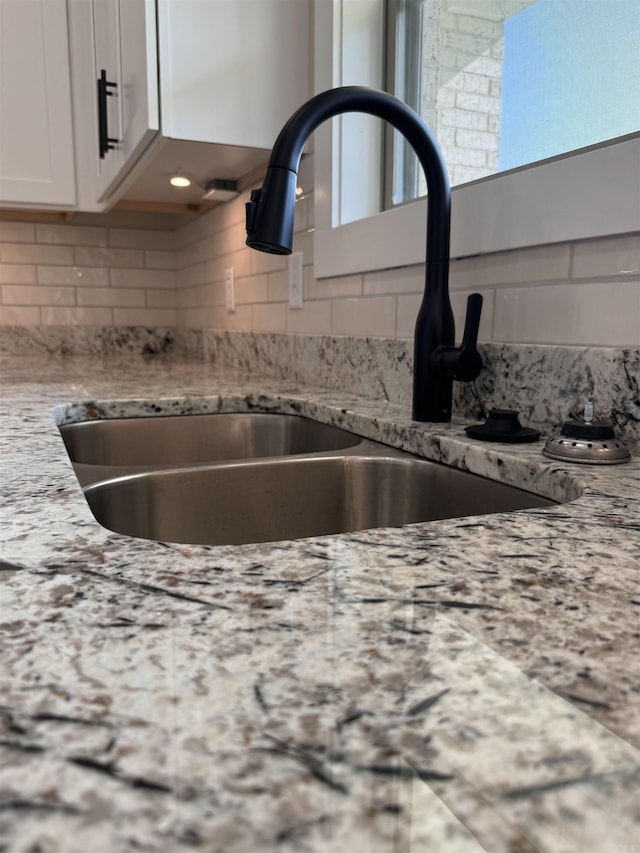 interior details featuring white cabinets, sink, light stone counters, and tasteful backsplash