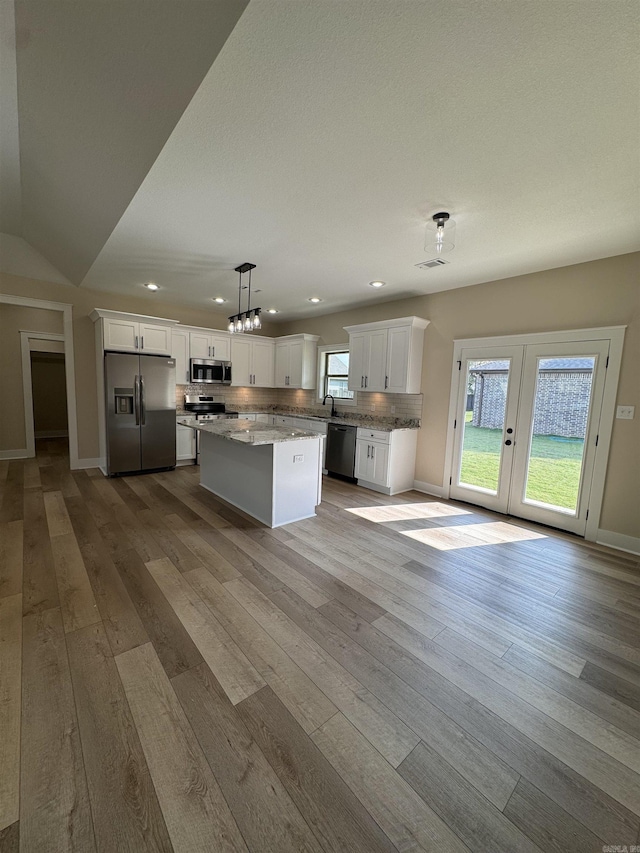 kitchen featuring stainless steel appliances, decorative light fixtures, a center island, white cabinets, and tasteful backsplash