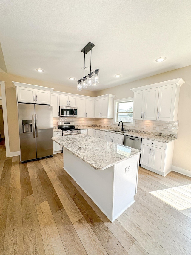 kitchen with white cabinets, stainless steel appliances, a kitchen island, sink, and decorative light fixtures