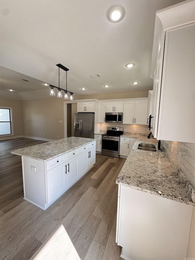 kitchen featuring stainless steel appliances, white cabinets, a center island, light wood-type flooring, and hanging light fixtures