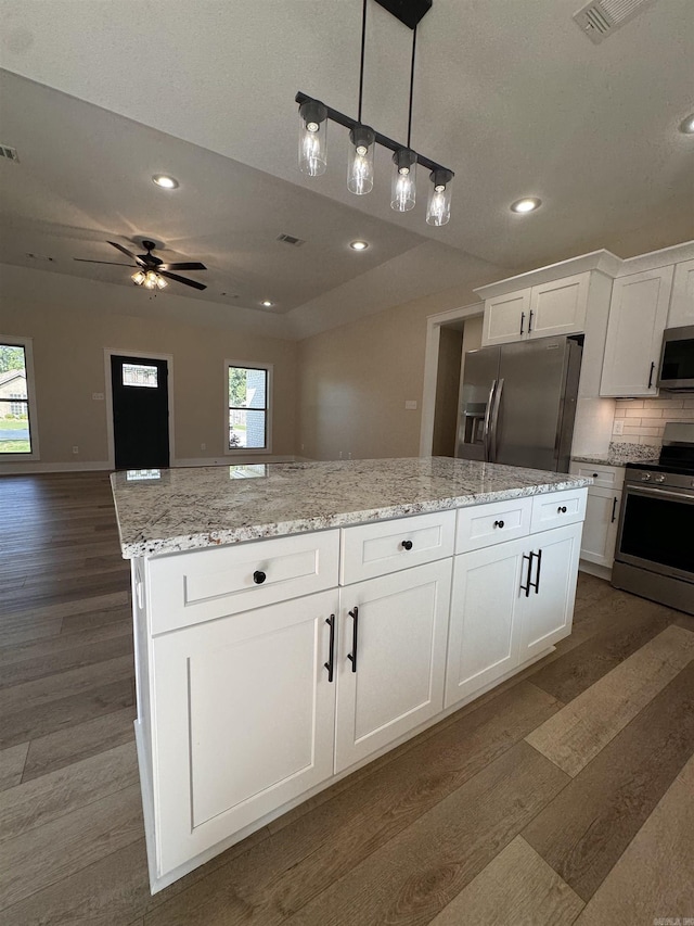 kitchen featuring stainless steel appliances, white cabinetry, ceiling fan, decorative backsplash, and a kitchen island