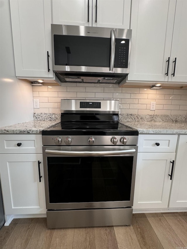 kitchen featuring light stone countertops, light hardwood / wood-style floors, tasteful backsplash, white cabinetry, and appliances with stainless steel finishes