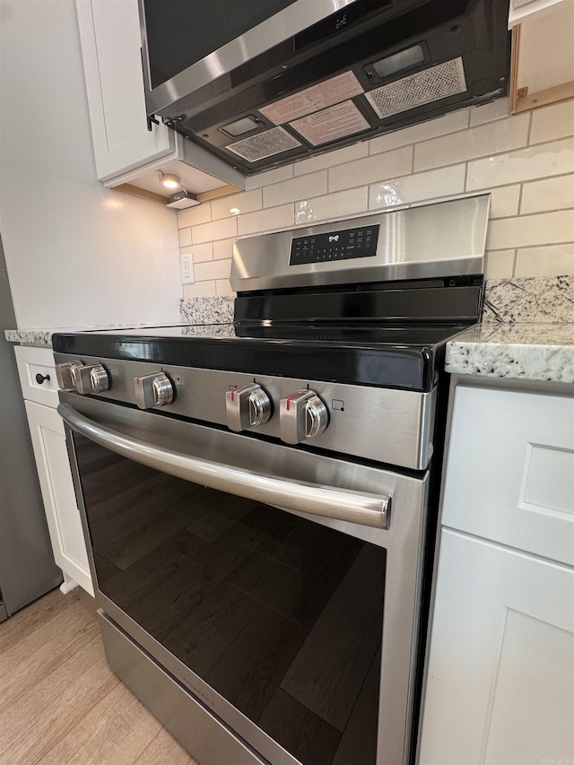 kitchen featuring white cabinets, light stone counters, light hardwood / wood-style floors, decorative backsplash, and appliances with stainless steel finishes