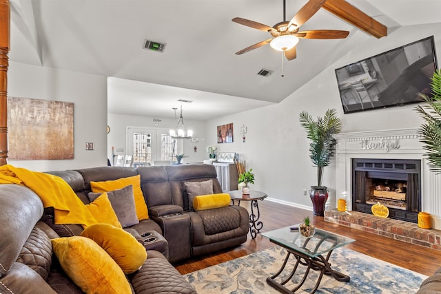 living room featuring a brick fireplace, vaulted ceiling with beams, ceiling fan with notable chandelier, and wood-type flooring