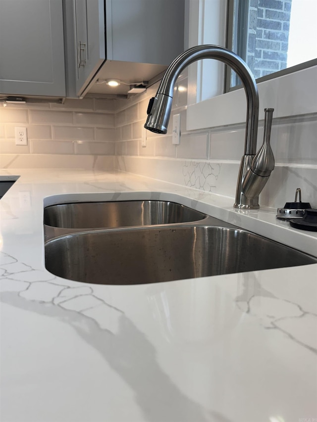 details featuring light stone counters, gray cabinets, tasteful backsplash, and sink