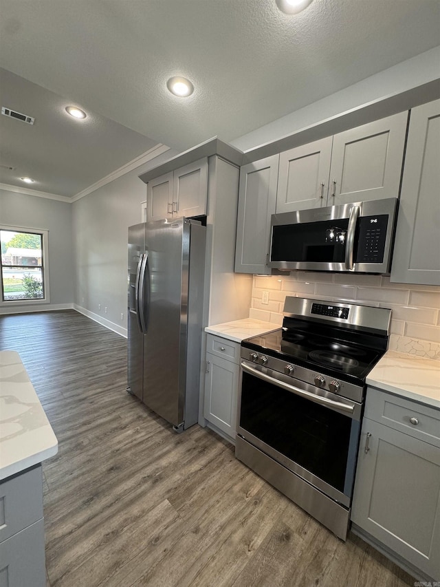 kitchen with light stone counters, dark hardwood / wood-style floors, stainless steel appliances, gray cabinets, and backsplash