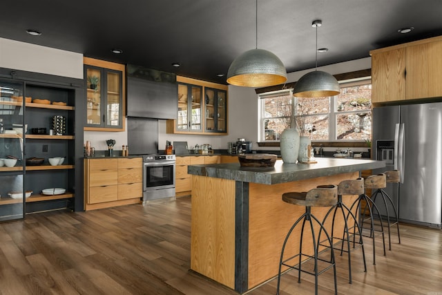 kitchen featuring stainless steel appliances, wall chimney exhaust hood, hanging light fixtures, a kitchen island, and dark hardwood / wood-style flooring