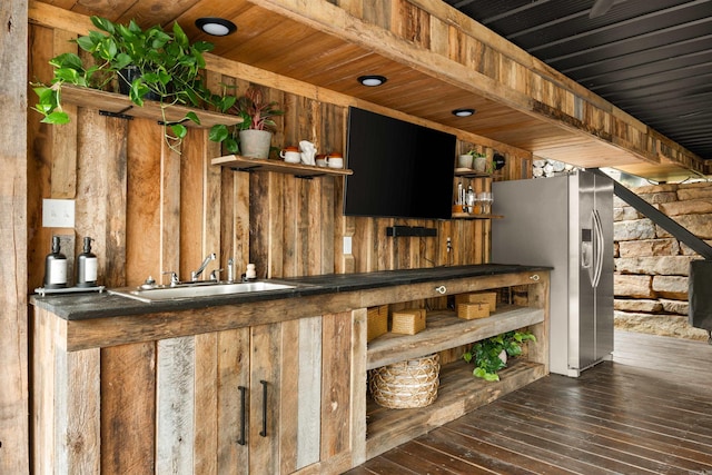 bar featuring sink, wooden walls, stainless steel fridge with ice dispenser, and dark hardwood / wood-style floors