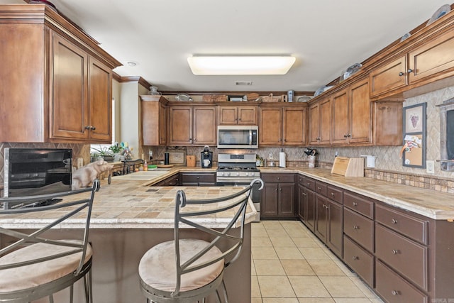 kitchen with a breakfast bar area, appliances with stainless steel finishes, kitchen peninsula, sink, and light tile patterned flooring