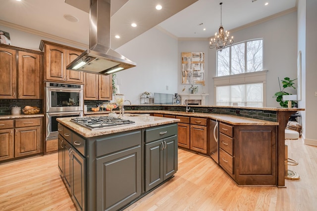 kitchen with a center island with sink, crown molding, light hardwood / wood-style flooring, appliances with stainless steel finishes, and island range hood