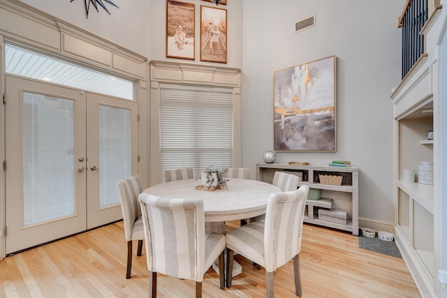 dining space featuring light hardwood / wood-style floors, a towering ceiling, and french doors