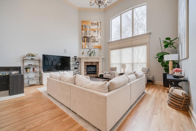 living room with light hardwood / wood-style floors, a healthy amount of sunlight, ornamental molding, a high end fireplace, and a chandelier