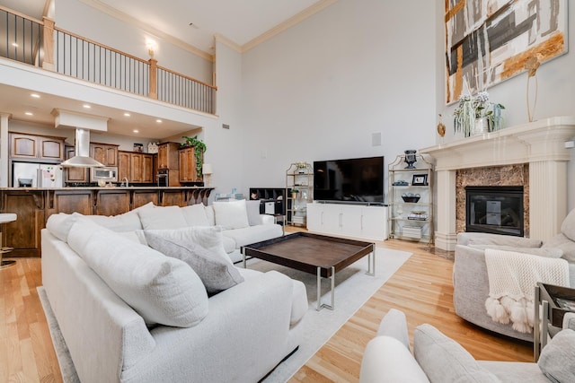 living room featuring a high ceiling, crown molding, a premium fireplace, and light wood-type flooring