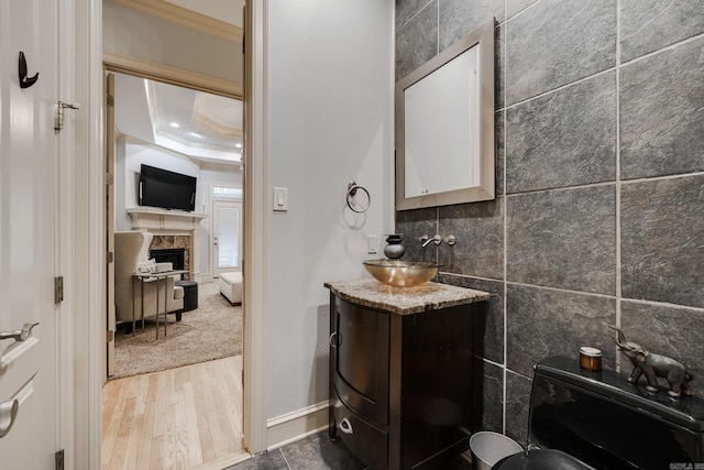 bathroom with hardwood / wood-style floors, a raised ceiling, a tiled fireplace, ornamental molding, and vanity