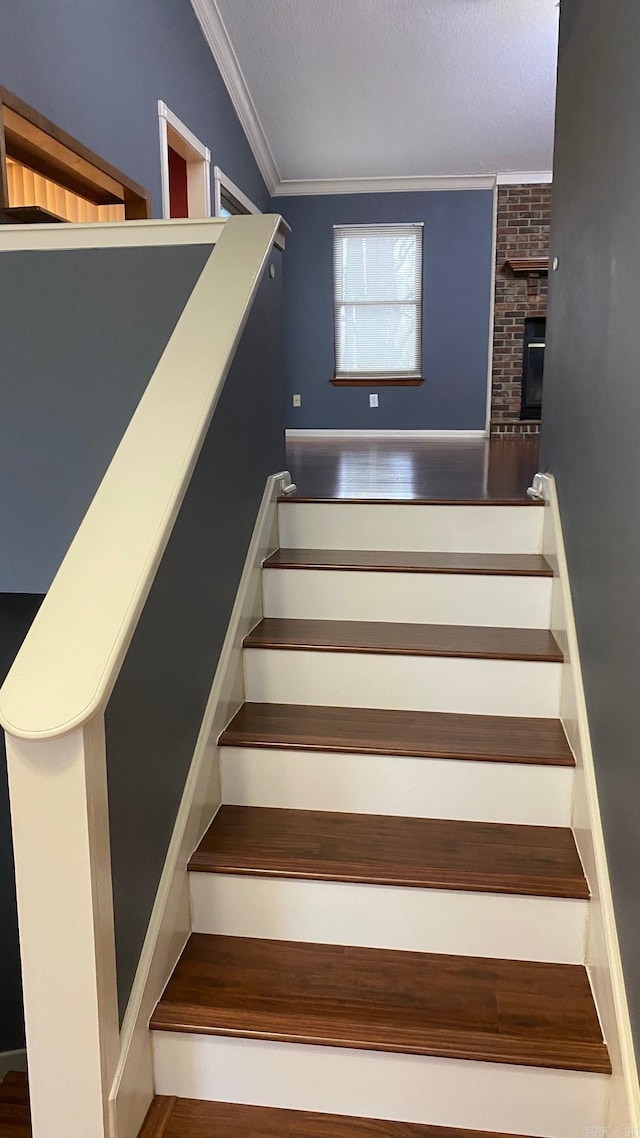 staircase featuring a brick fireplace, crown molding, and hardwood / wood-style flooring