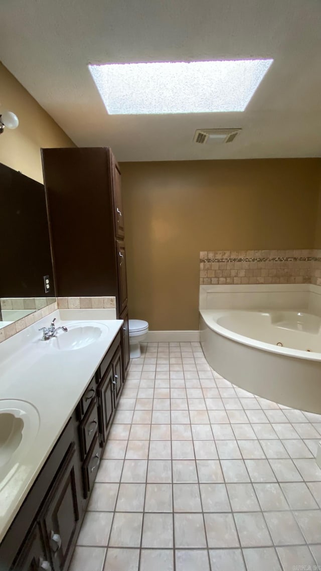 bathroom with toilet, a washtub, tile patterned flooring, a skylight, and vanity