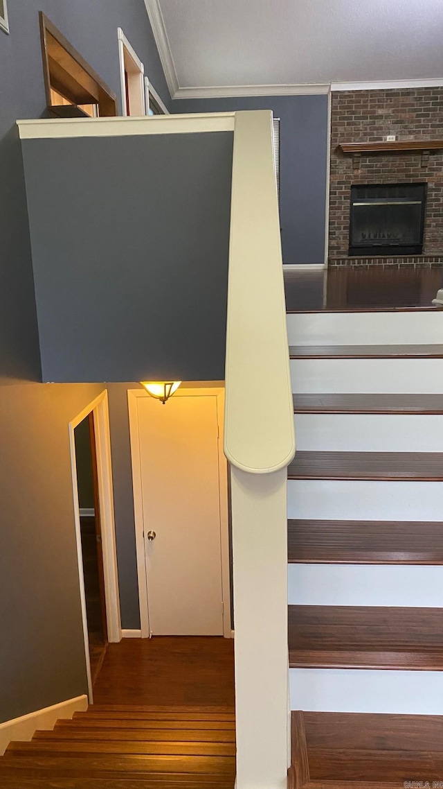 stairway featuring ornamental molding, a brick fireplace, and wood-type flooring