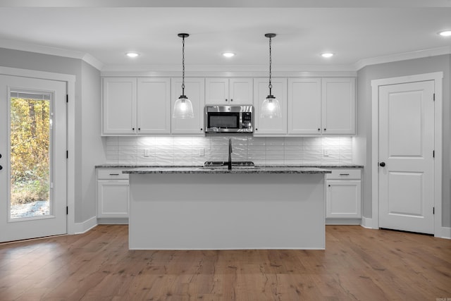 kitchen with an island with sink, tasteful backsplash, light stone countertops, pendant lighting, and white cabinets