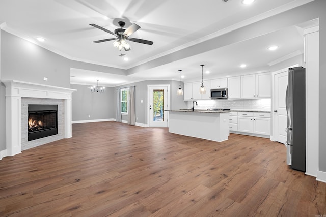 kitchen featuring pendant lighting, appliances with stainless steel finishes, white cabinetry, a fireplace, and a center island with sink