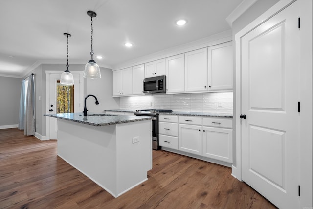 kitchen featuring white cabinetry, a center island with sink, appliances with stainless steel finishes, dark stone countertops, and hanging light fixtures