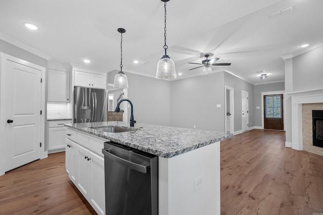 kitchen with white cabinetry, stainless steel appliances, sink, a kitchen island with sink, and a tile fireplace