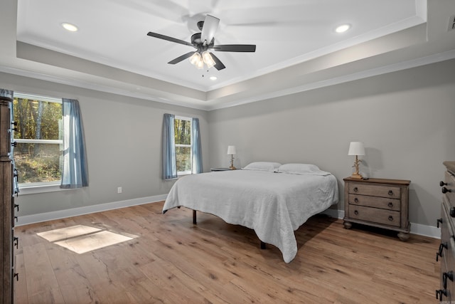 bedroom with a raised ceiling, ceiling fan, light wood-type flooring, and multiple windows