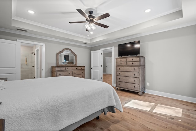 bedroom featuring ceiling fan, ensuite bathroom, light hardwood / wood-style floors, and a tray ceiling