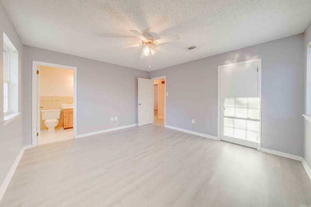 unfurnished bedroom with a textured ceiling, ceiling fan, light hardwood / wood-style flooring, and ensuite bath