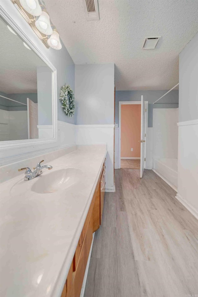 bathroom featuring wood-type flooring, a textured ceiling, walk in shower, and vanity