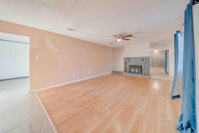 unfurnished living room featuring ceiling fan, a brick fireplace, a textured ceiling, and light hardwood / wood-style floors