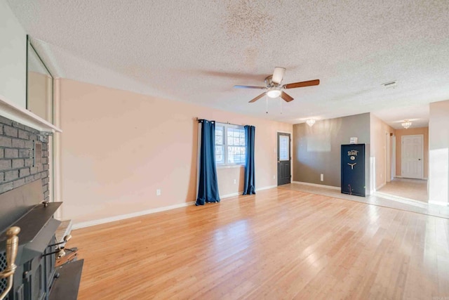 unfurnished living room with ceiling fan, a brick fireplace, a textured ceiling, and light hardwood / wood-style floors