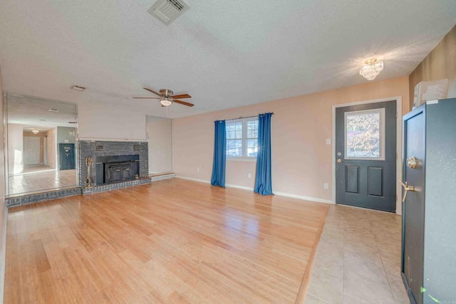 unfurnished living room featuring a textured ceiling, ceiling fan, wood-type flooring, and a brick fireplace