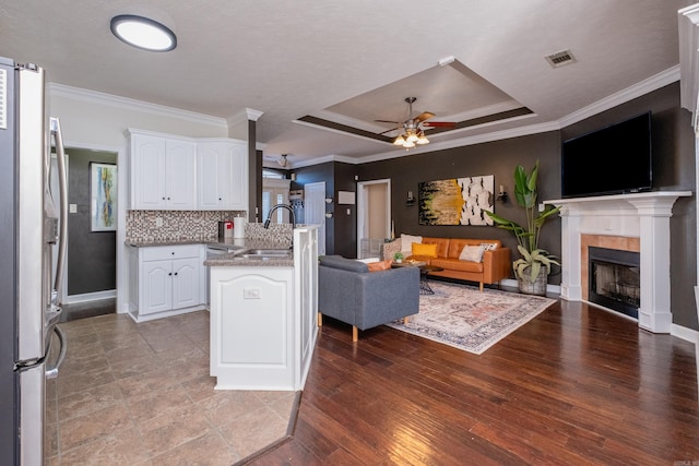 kitchen featuring stainless steel fridge, kitchen peninsula, a tray ceiling, white cabinets, and sink