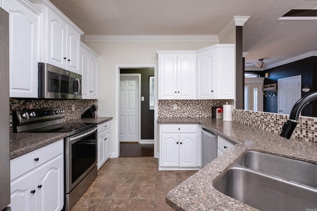 kitchen featuring appliances with stainless steel finishes, dark stone counters, ornamental molding, white cabinets, and sink