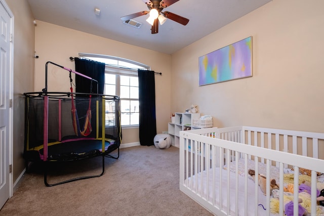 bedroom featuring ceiling fan, light colored carpet, and a nursery area