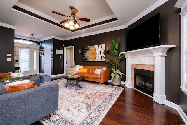 living room with dark hardwood / wood-style floors, ornamental molding, ceiling fan, a tray ceiling, and a tile fireplace