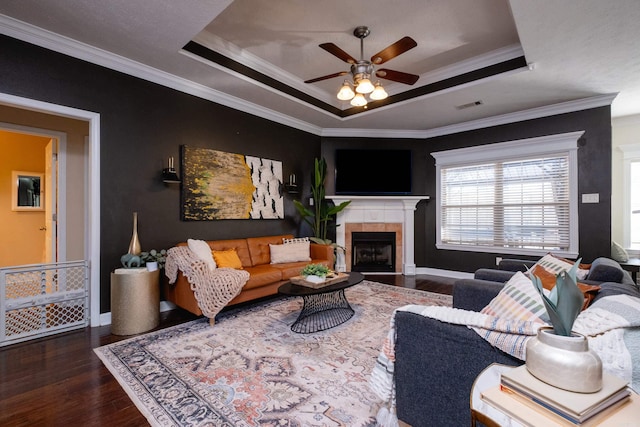 living room featuring a tiled fireplace, hardwood / wood-style floors, crown molding, and a raised ceiling