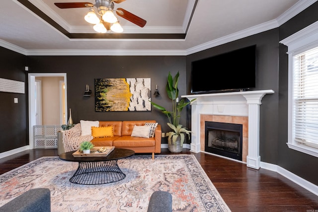 living room featuring dark hardwood / wood-style floors, a raised ceiling, ornamental molding, and a tiled fireplace