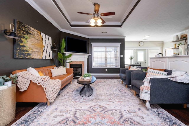 living room with a raised ceiling, ceiling fan, a fireplace, and ornamental molding