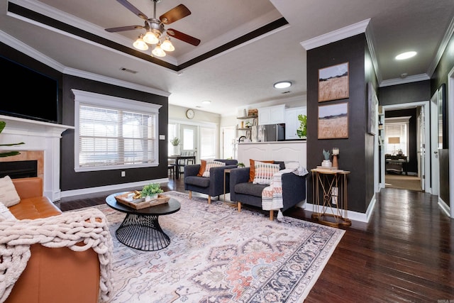 living room with ceiling fan, crown molding, a raised ceiling, and dark hardwood / wood-style floors