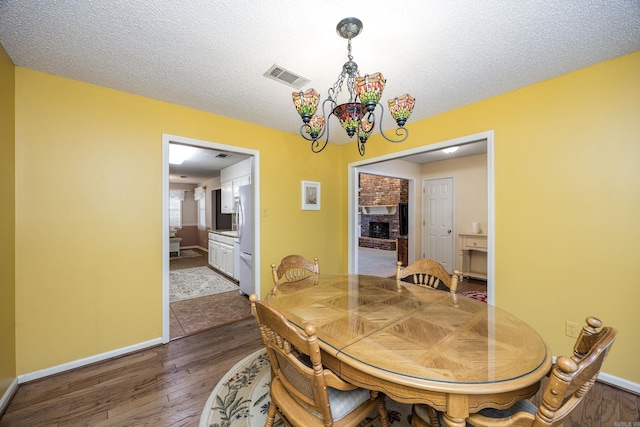 dining area featuring a textured ceiling, a brick fireplace, dark hardwood / wood-style flooring, and a chandelier