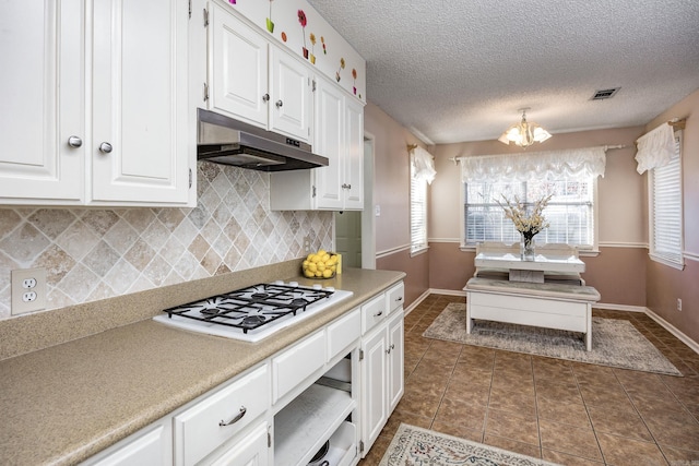 kitchen with a notable chandelier, white cabinetry, dark tile patterned floors, a textured ceiling, and white gas stovetop