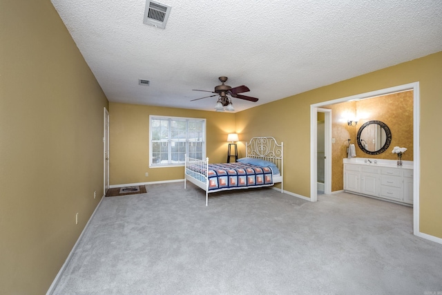 bedroom featuring a textured ceiling, ceiling fan, light carpet, and ensuite bath