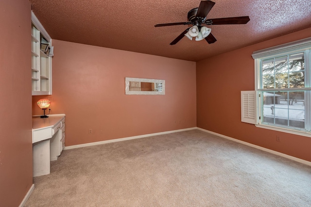 empty room with ceiling fan, light colored carpet, a textured ceiling, and built in desk