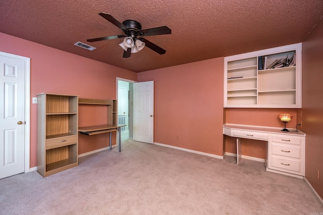 unfurnished office featuring light carpet, ceiling fan, built in desk, and a textured ceiling