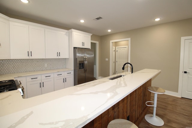 kitchen featuring stainless steel appliances, a kitchen bar, white cabinetry, and light stone counters