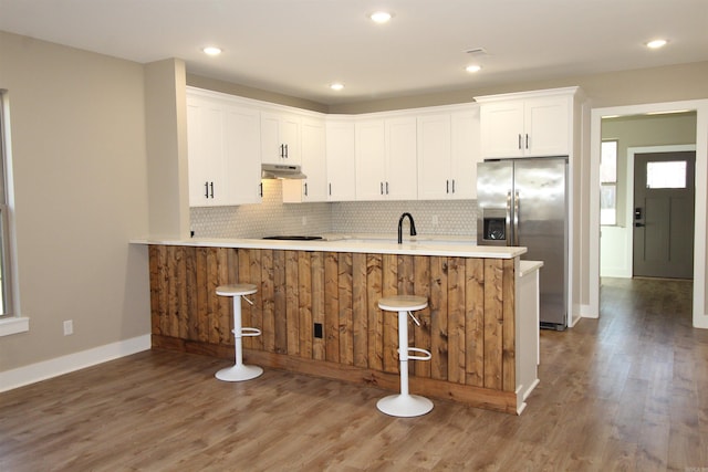 kitchen featuring kitchen peninsula, white cabinets, stainless steel refrigerator with ice dispenser, and a breakfast bar