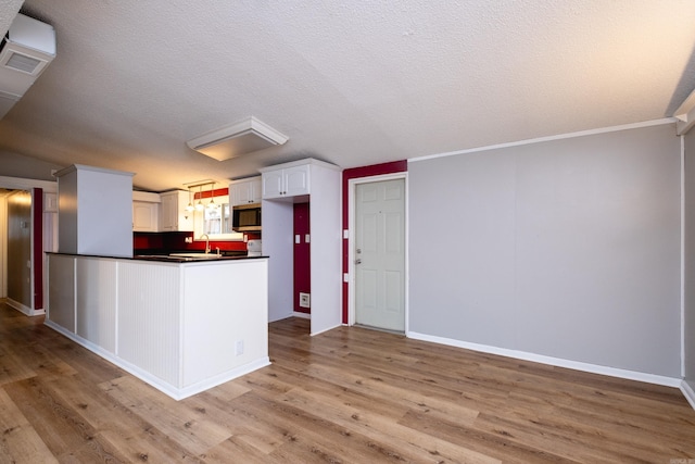 kitchen with decorative light fixtures, crown molding, white cabinetry, light wood-type flooring, and a textured ceiling