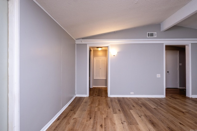 spare room with lofted ceiling with beams, a textured ceiling, and light hardwood / wood-style flooring